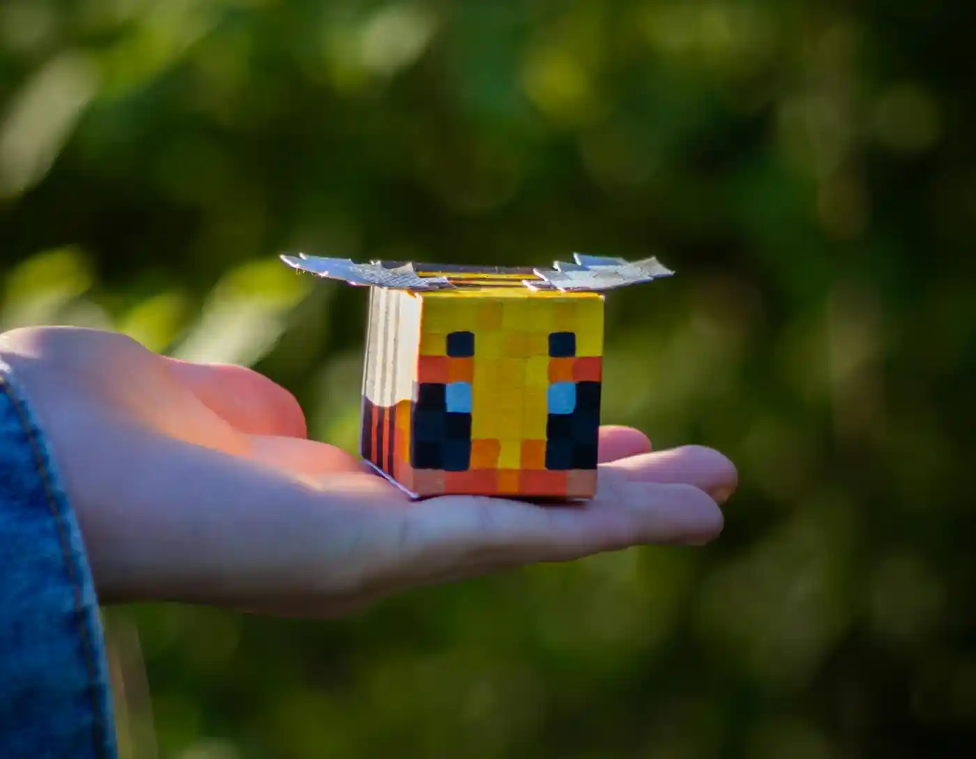 Pszczoła zrobiona z sześcianu Pszczola stworozna z kartonu leżąca na dłoni młodego człowieka. Rękodzieło nawiązuje prawdopodobnie do popularnej gry minecraft.