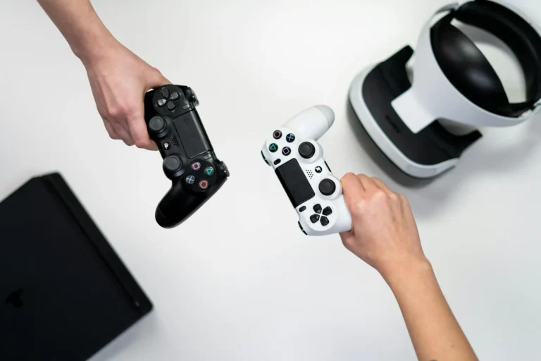 Para rąk, jedna ręka trzyma czarny dżojstik do ps4, a druga biały. Zdjęcie jest bardzo kontrastujące czarny z białym.