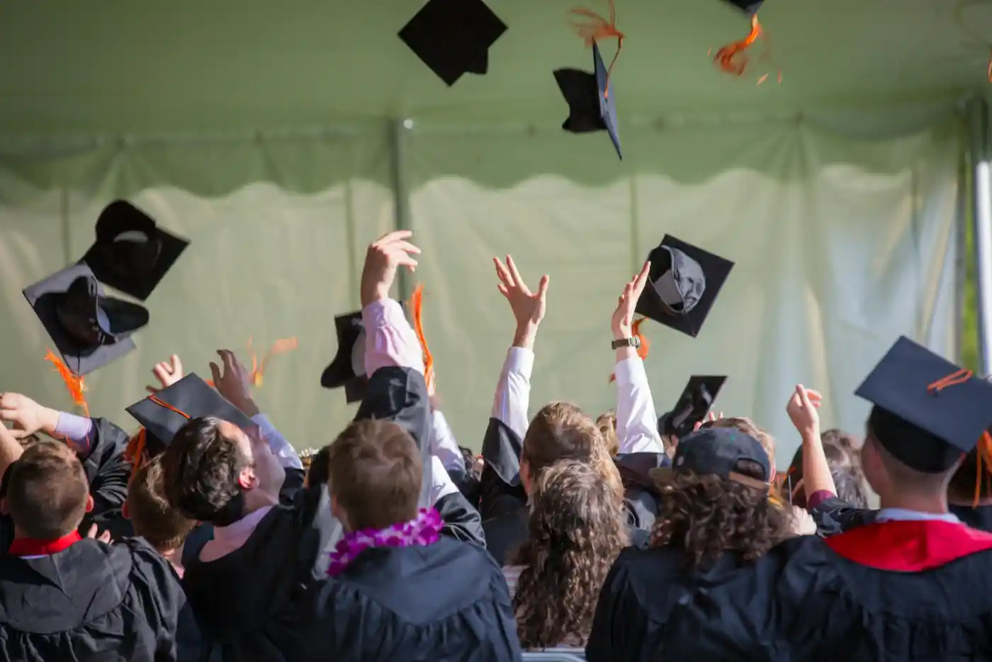 Graduacja studentów, studenci wyrzucają w powietrze swoje birety, mają na twarzach uśmiech, jest wiele osób.